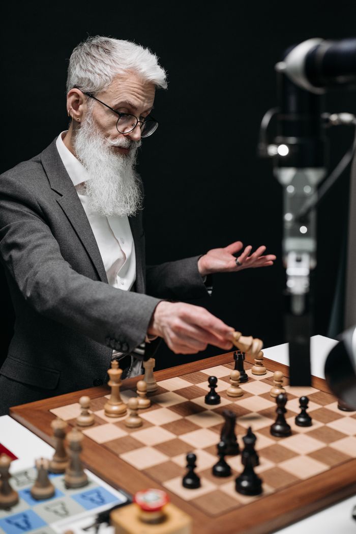 Elderly man engages in a strategic chess game with a robotic arm, showcasing technology.